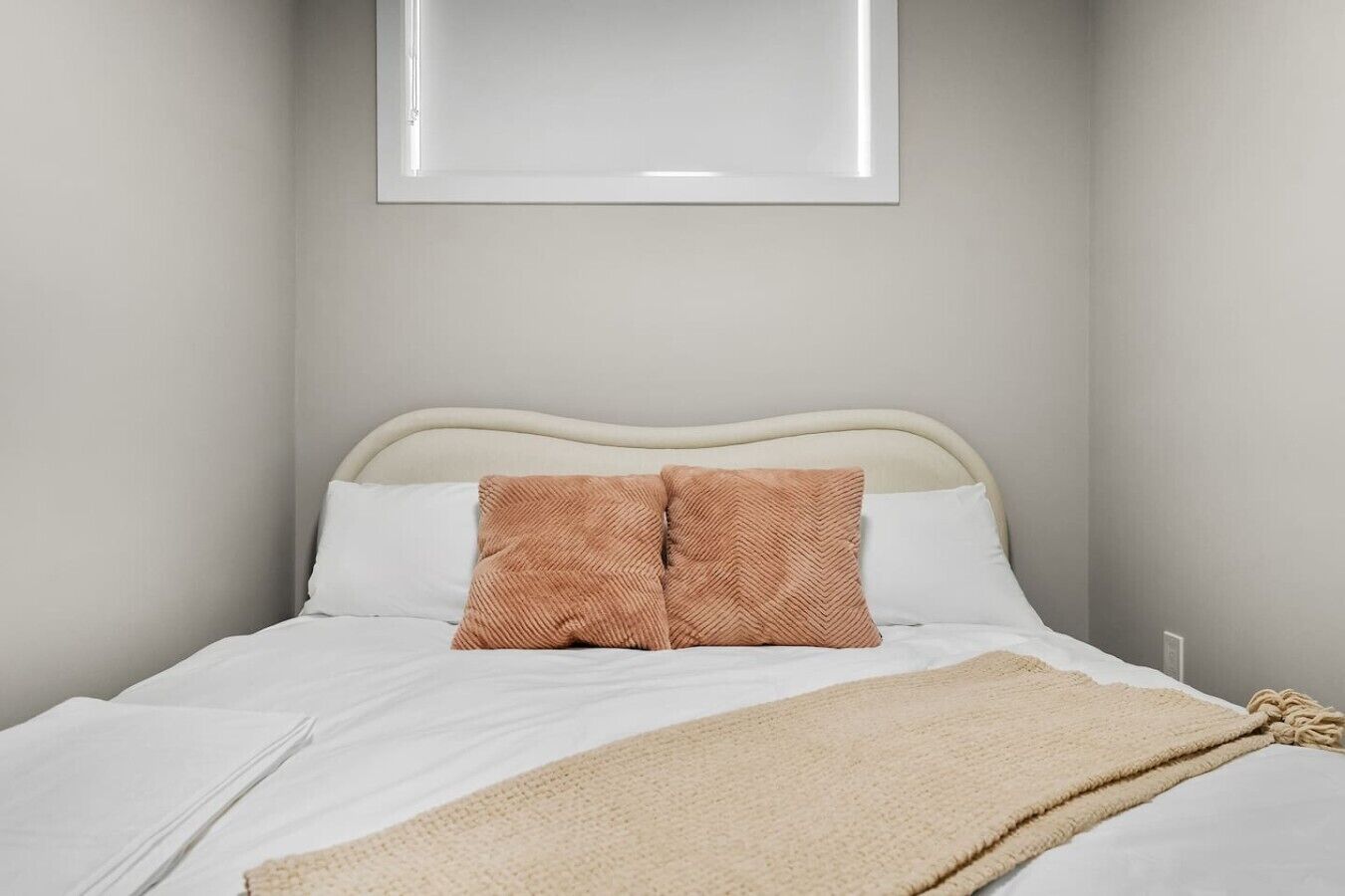 Una cama con ropa de cama blanca, dos almohadas marrones y una manta color beige.
