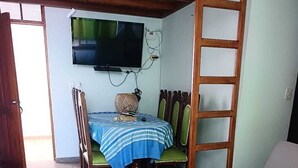 Ein Zimmer mit Esstisch, Stühlen, einem an der Wand montierten Fernseher, einer Couch und einer Holzleiter.