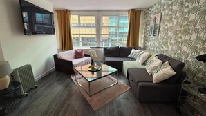 Un salon moderne avec un canapé, un fauteuil et une table basse, un radiateur et un téléviseur fixé au mur.