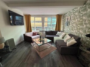 Ein modernes Wohnzimmer mit Sofa, Sessel und Couchtisch, einem Heizkörper sowie einem an der Wand befestigten Fernseher.