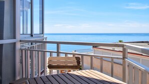 En balkon med udsigt over havet, træmøbler og gelænder i hvidt.