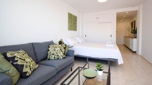 En moderne stue med sofa, seng, sofabord i glas og en lille plante.