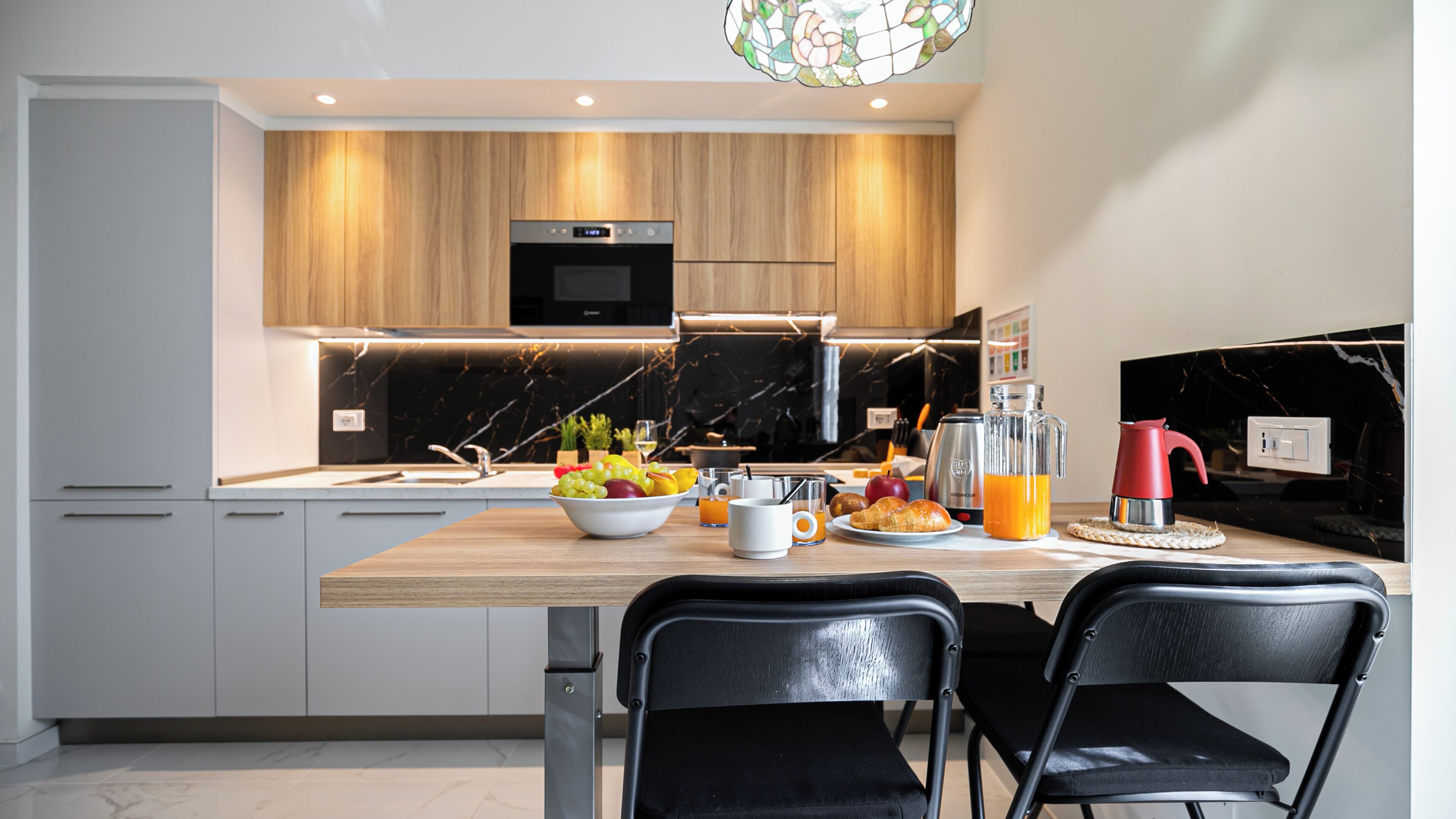 Una cocina moderna con encimera de madera, un bol de fruta, una cafetera y un hervidor rojo.