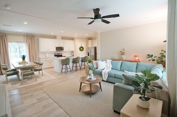 A modern living room with a sofa, a coffee table, and a dining area with chairs and a table.