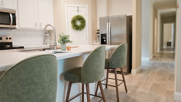 Uma cozinha moderna com armários brancos, uma ilha central com banquetas, micro-ondas, geladeira e uma guirlanda decorativa.