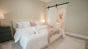 Quarto com cama grande, mesa de cabeceira, cômoda e porta corrediça tipo celeiro.