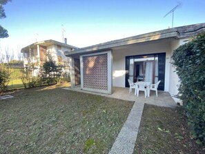 Ein Wohnhaus mit überdachter Terrasse, kleinem Rasen und einer zur Garage führenden Tür.