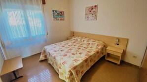 Un dormitorio con cama, mesita de noche, cortinas en una ventana y dos cuadros en la pared.