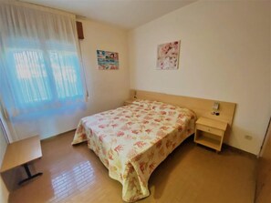 Ein Schlafzimmer mit Bett, Nachttisch, Vorhängen am Fenster und zwei Bildern an der Wand.