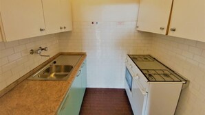 Una cocina compacta con gabinetes blancos, un lavamanos de acero inoxidable, una estufa a gas y un salpicadero azulejado.