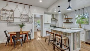 Una cucina moderna con mobili bianchi, un tavolo da pranzo in legno, lampade a sospensione e una grande isola con sgabelli da bar.