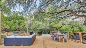 Un patio di legno con divano e tavolo, immerso nel verde.