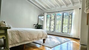 Ein Schlafzimmer mit Bett, Holzboden, großen Fenstern und einem Oberlicht.