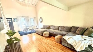Ein Wohnzimmer mit Holzboden, einem Ecksofa, einem Couchtisch und einer Pflanze.