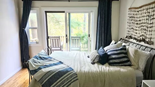 Ein Schlafzimmer mit Bett, einem Fenster mit Vorhängen, einer Balkontür und einem an der Wand befestigten Vogelhaus.