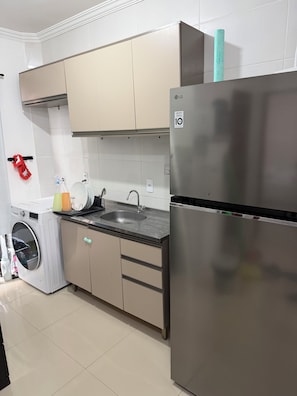 A kitchen with a stainless steel refrigerator, a washing machine, a sink, and cabinets.