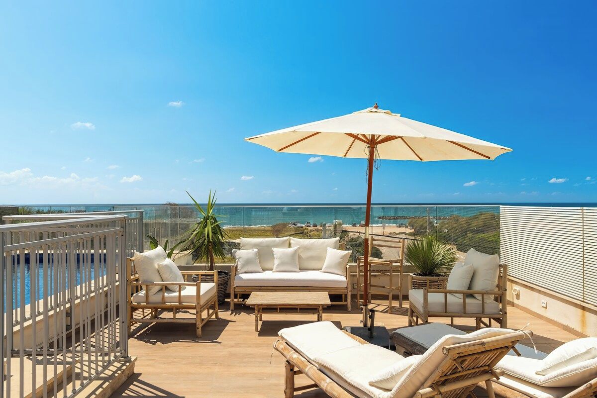 A rooftop terrace with a pool, lounge chairs, a sofa, and a large umbrella.
