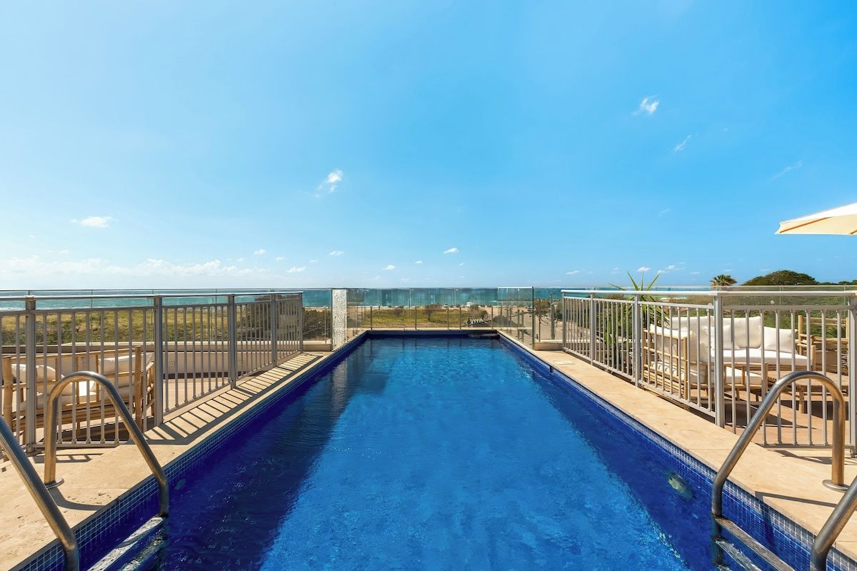 A swimming pool with a view of the ocean, surrounded by a metal railing and lounge chairs.