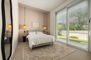 A bedroom with a bed, bedside tables, a large window, and a view of the outdoors.