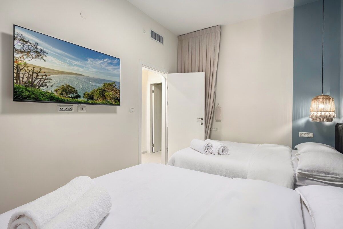 A hotel room with a bed, a TV mounted on the wall, a door, and a hanging light fixture.
