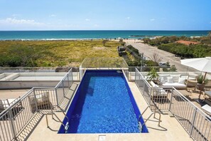 Ein Pool auf dem Dach mit Blick auf das Meer, umgeben von Sitzgelegenheiten im Freien und einem Zaun.