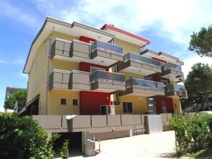 Ein mehrstöckiges Gebäude mit Balkonen, einer flachen Dachterrasse und einem verschlossenen Eingang.
