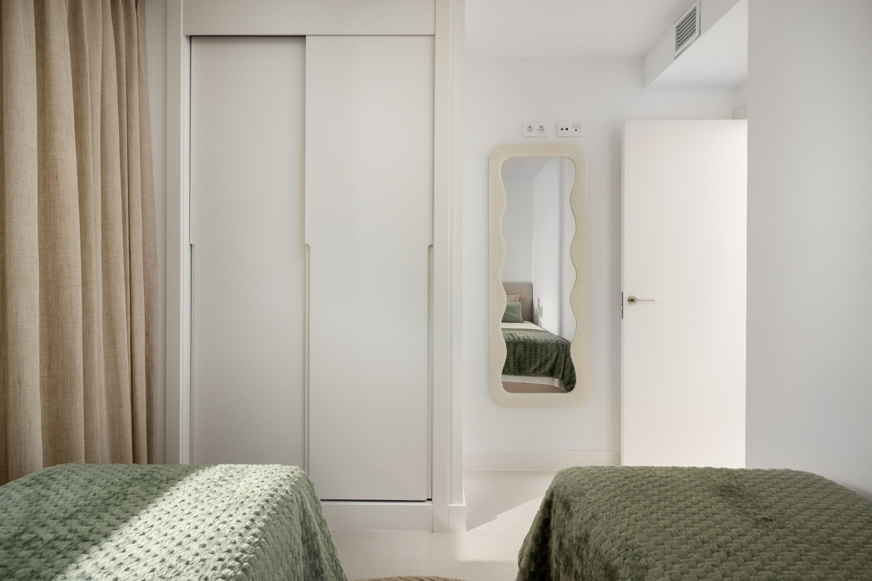 A bedroom with a wardrobe, a mirror, and two beds.