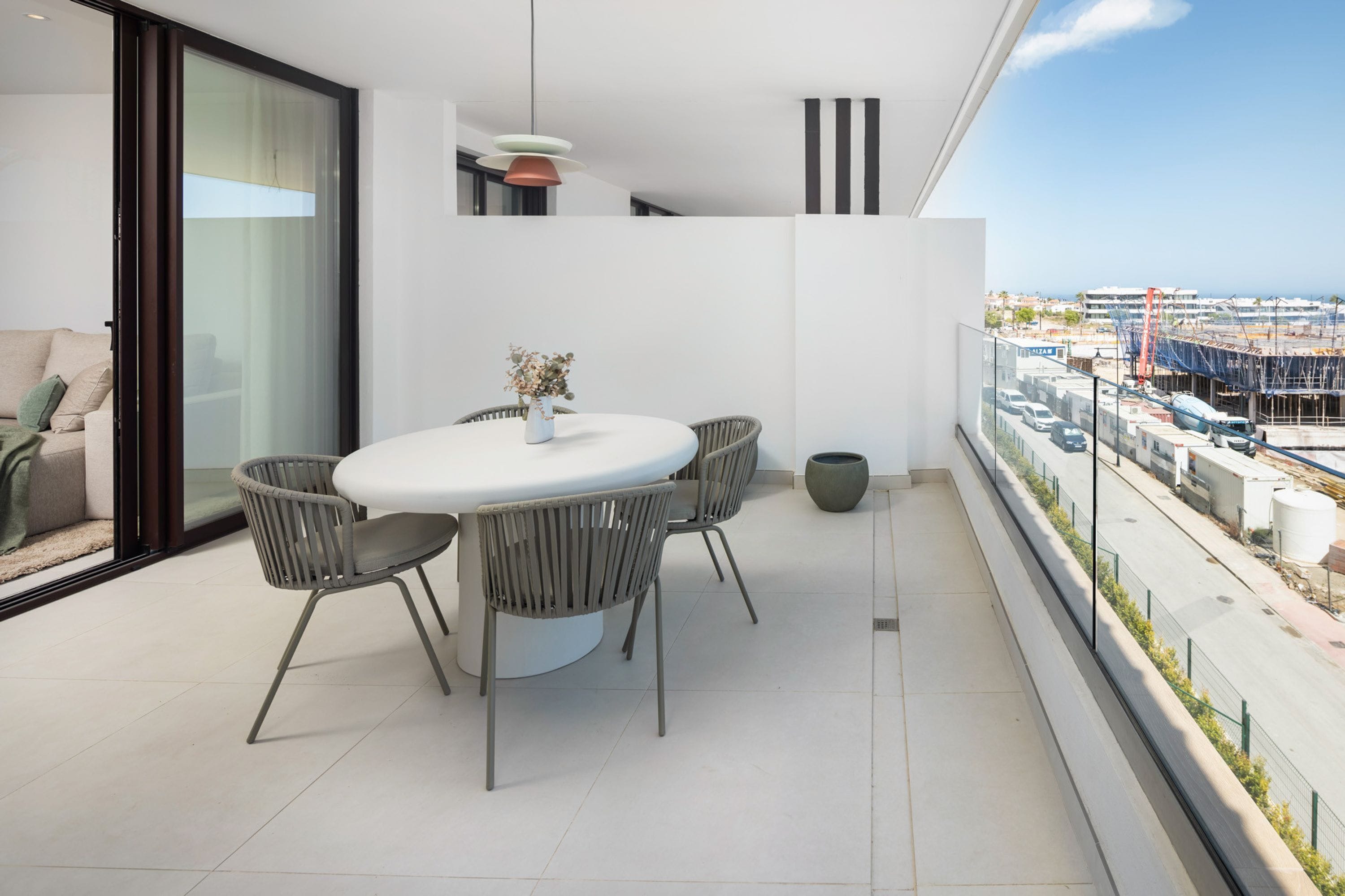 Un balcon moderne avec une table et des chaises pour les repas, un canapé et une vue sur un chantier de construction.