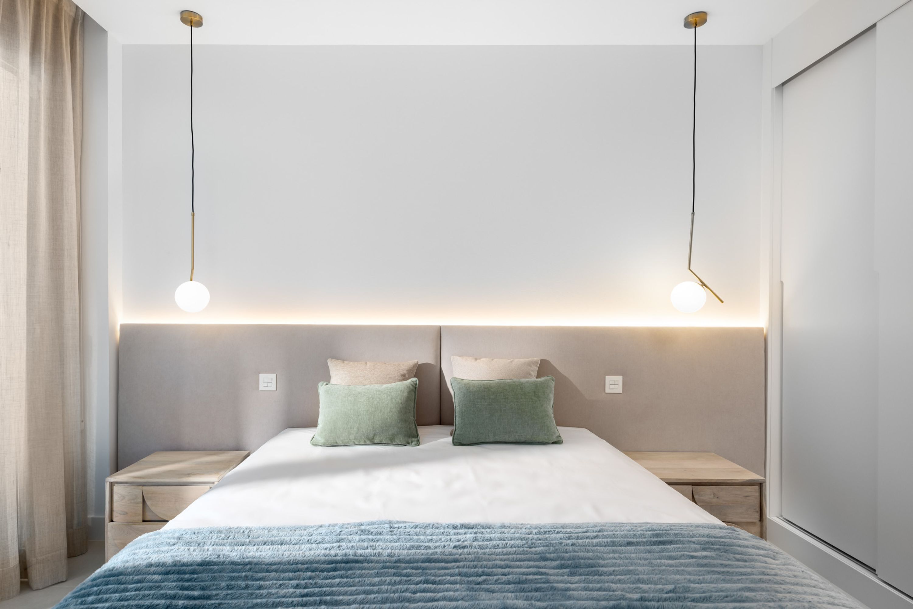 A modern bedroom with a large bed, bedside tables, and a headboard with integrated lighting.