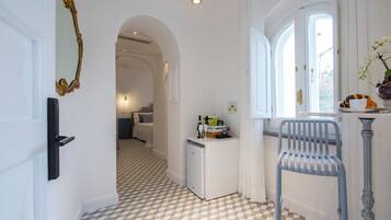 A hallway with a checkered floor, a refrigerator, a chair, and a window with curtains.
