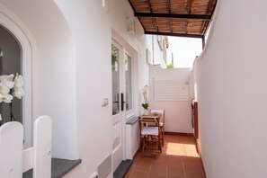 A narrow corridor with a door, a window, a small table with chairs, and a tiled floor. - CASA LUCIA RELAXING ROOMS (Anacapri)
