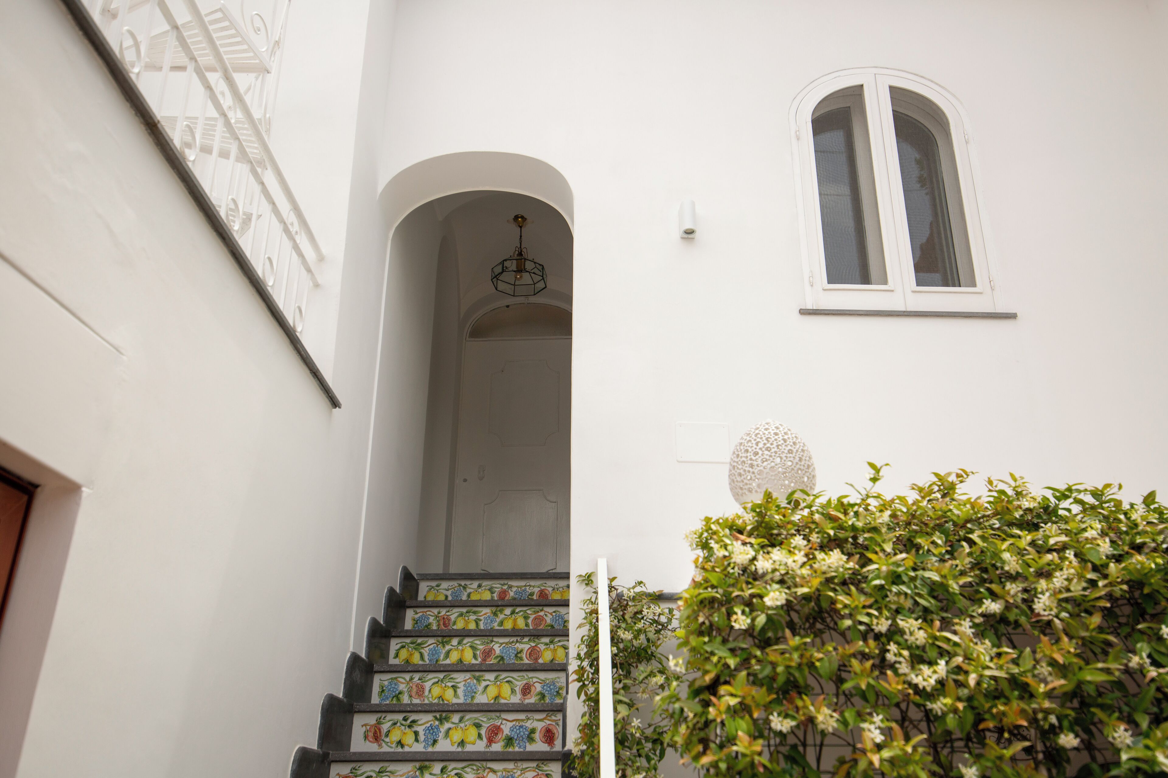 Eine Treppe mit bunten Stufen, eine weiße Wand, ein Fenster und eine Pflanze.