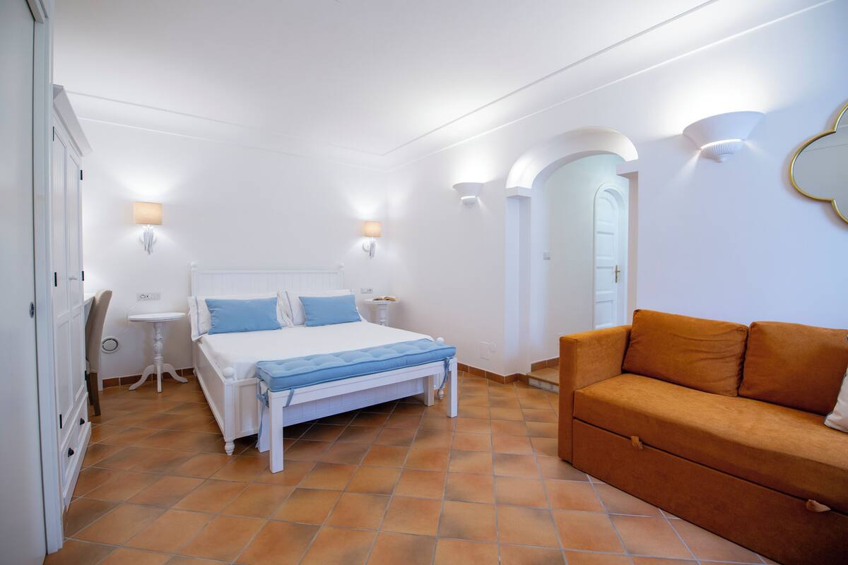 Un dormitorio con cama, sofá, escritorio y lámpara.