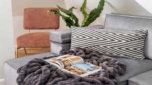 A modern living room with a grey sofa, a pink chair, a black and white patterned pillow, a large green plant, and a book on a grey blanket. - Casablanca - Near the Beach Sopot (Sopot)