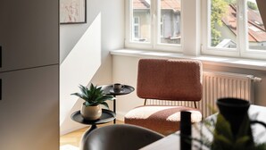 A cozy room with a window, a chair, a small table with a plant, and a framed picture on the wall. - Casablanca - Near the Beach Sopot (Sopot)