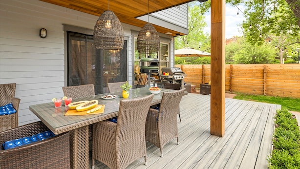 Un patio al aire libre con mesa de comedor, sillas de mimbre, luces colgantes y zona de barbacoa.