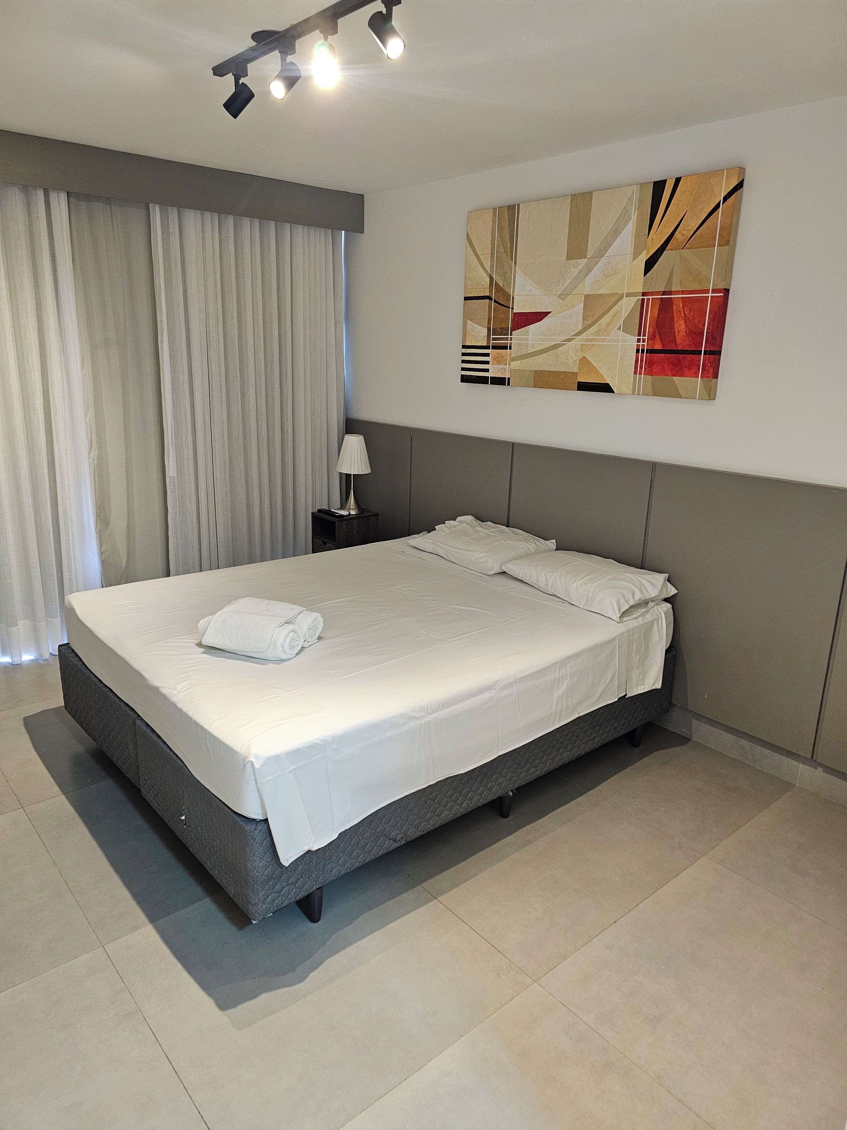 A modern hotel room with a large bed, a nightstand, a lamp, and a ceiling light fixture.