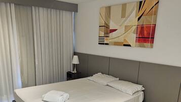 A modern hotel room with a large bed, a nightstand, a lamp, and a ceiling light fixture.