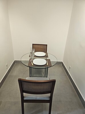A dining area with a round glass table, two chairs, and a white plate set. - Flat 109 Norte Novo e Completo 204 (Brasília)