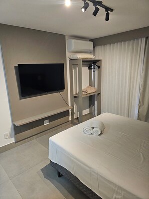 A modern hotel room with a bed, a flat-screen TV mounted on the wall, a built-in air conditioning unit, and a window with curtains. - Flat 109 Norte Novo e Completo 204 (Brasília)