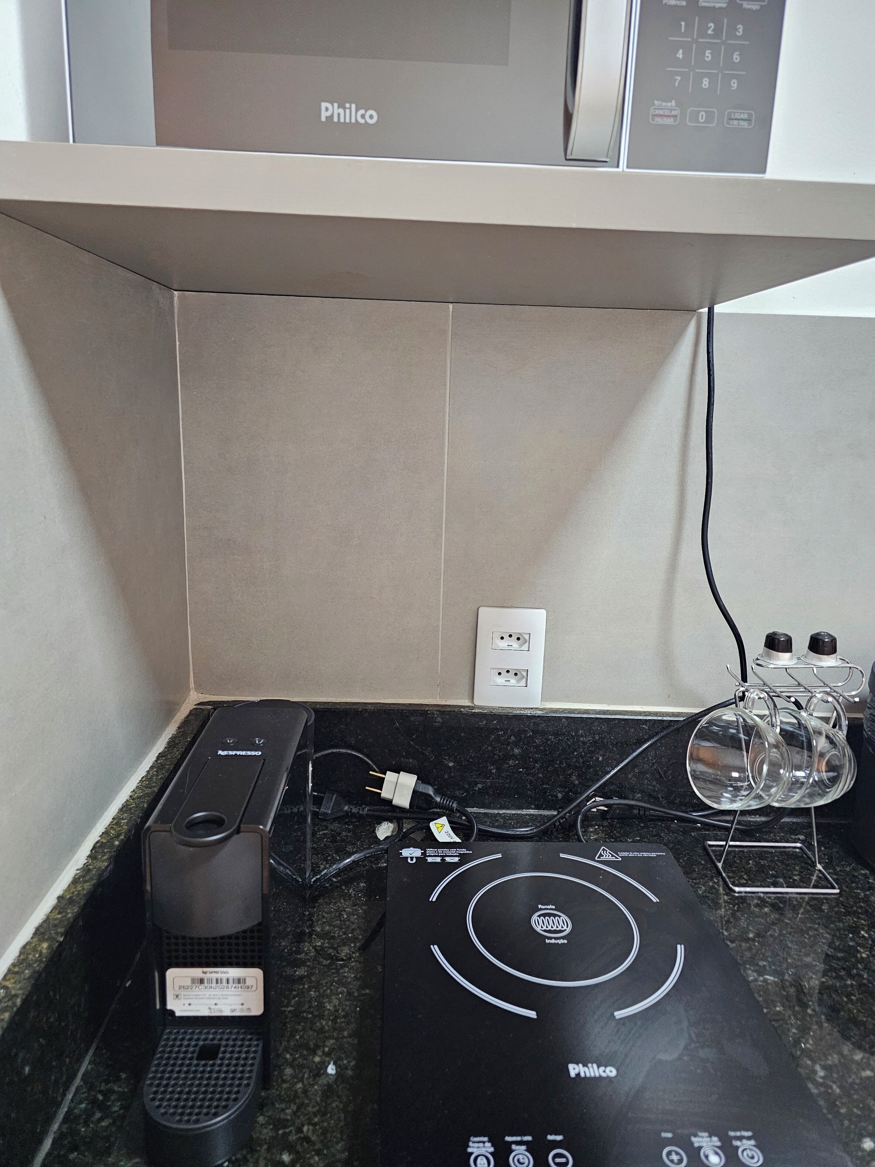 A kitchen with a coffee maker, a black appliance with a control panel, and a power strip with two plugs.
