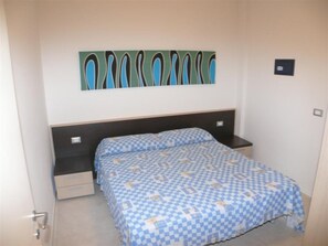 Ein Schlafzimmer mit einem Bett, einem Nachttisch, einer Schublade, einem Wandbild und einer Tür.