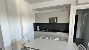Una cocina moderna con armarios blancos, microondas y cafetera. Hay una mesa de comedor con cuatro sillas.