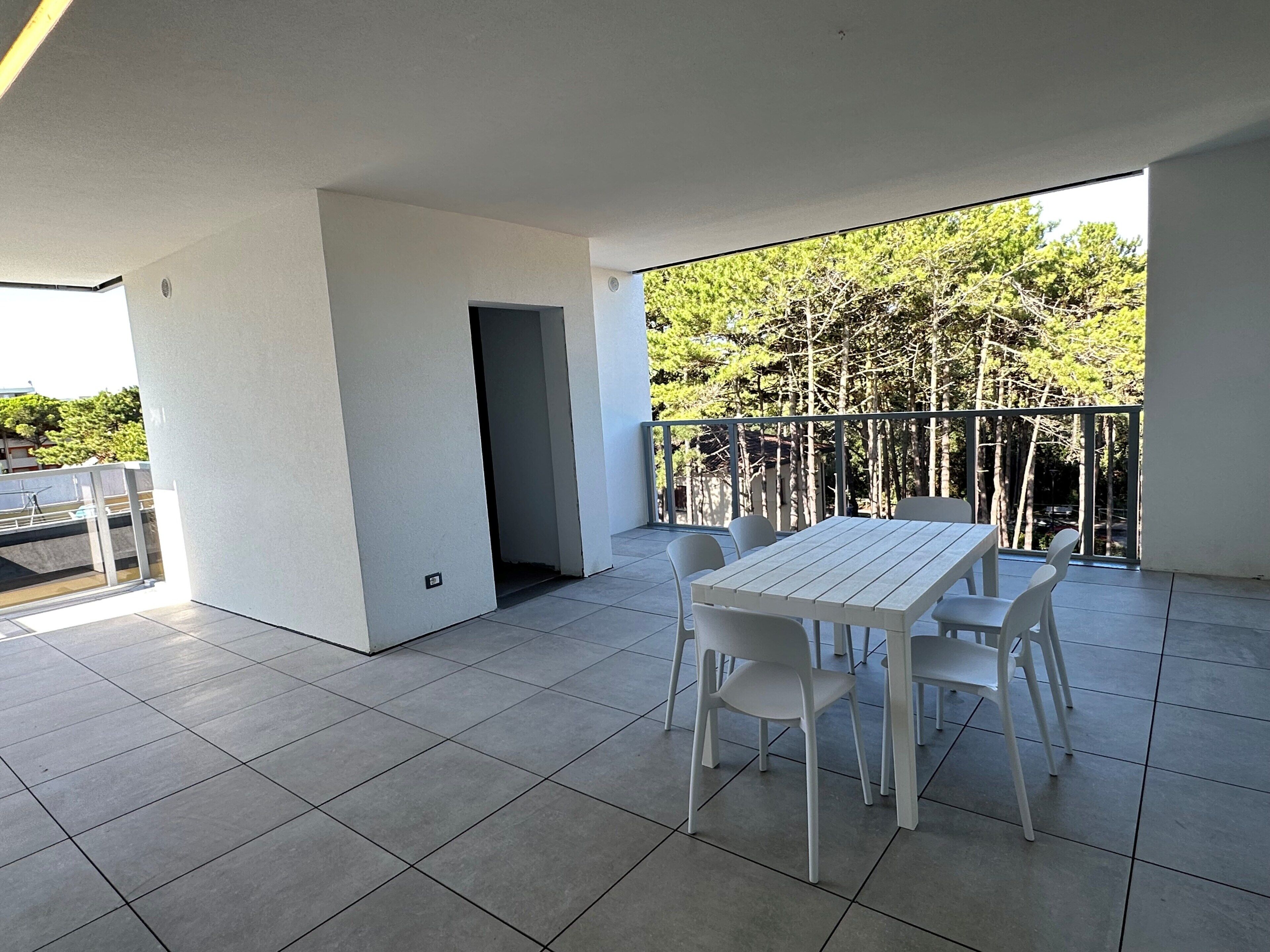 A balcony with a table and chairs, a view of trees, and a tiled floor.