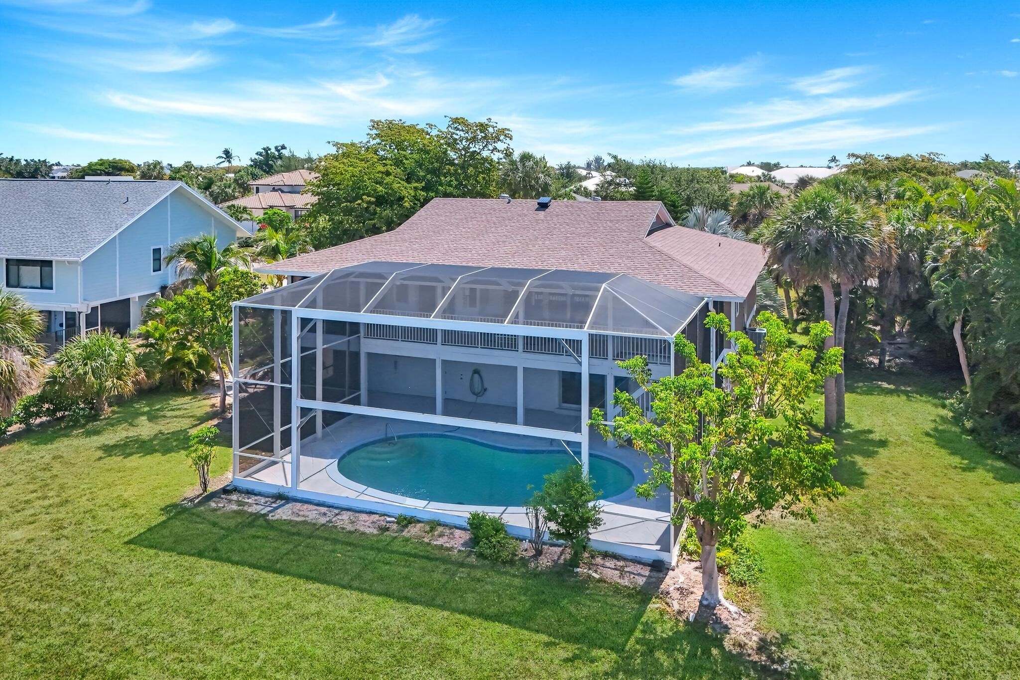 A house with a large glass-enclosed swimming pool, surrounded by a well-maintained lawn and trees.