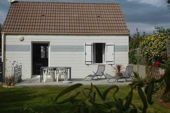 A single-story house with a tiled roof, a front door, and a small patio with two chairs and a table.