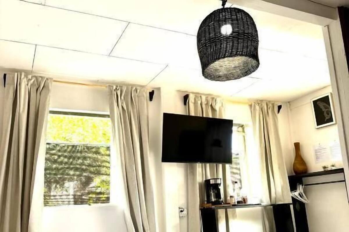 Habitación de hotel con cama, televisor, escritorio y cafetera, y ventana con cortinas.