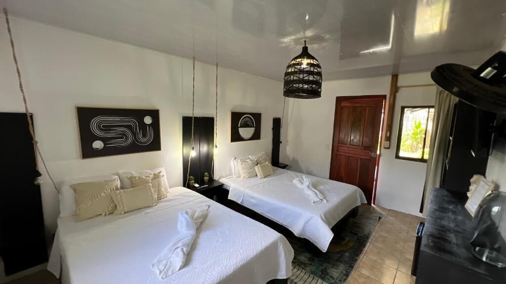 A hotel room with two beds, a wooden door, a black lamp, and artwork on the walls.