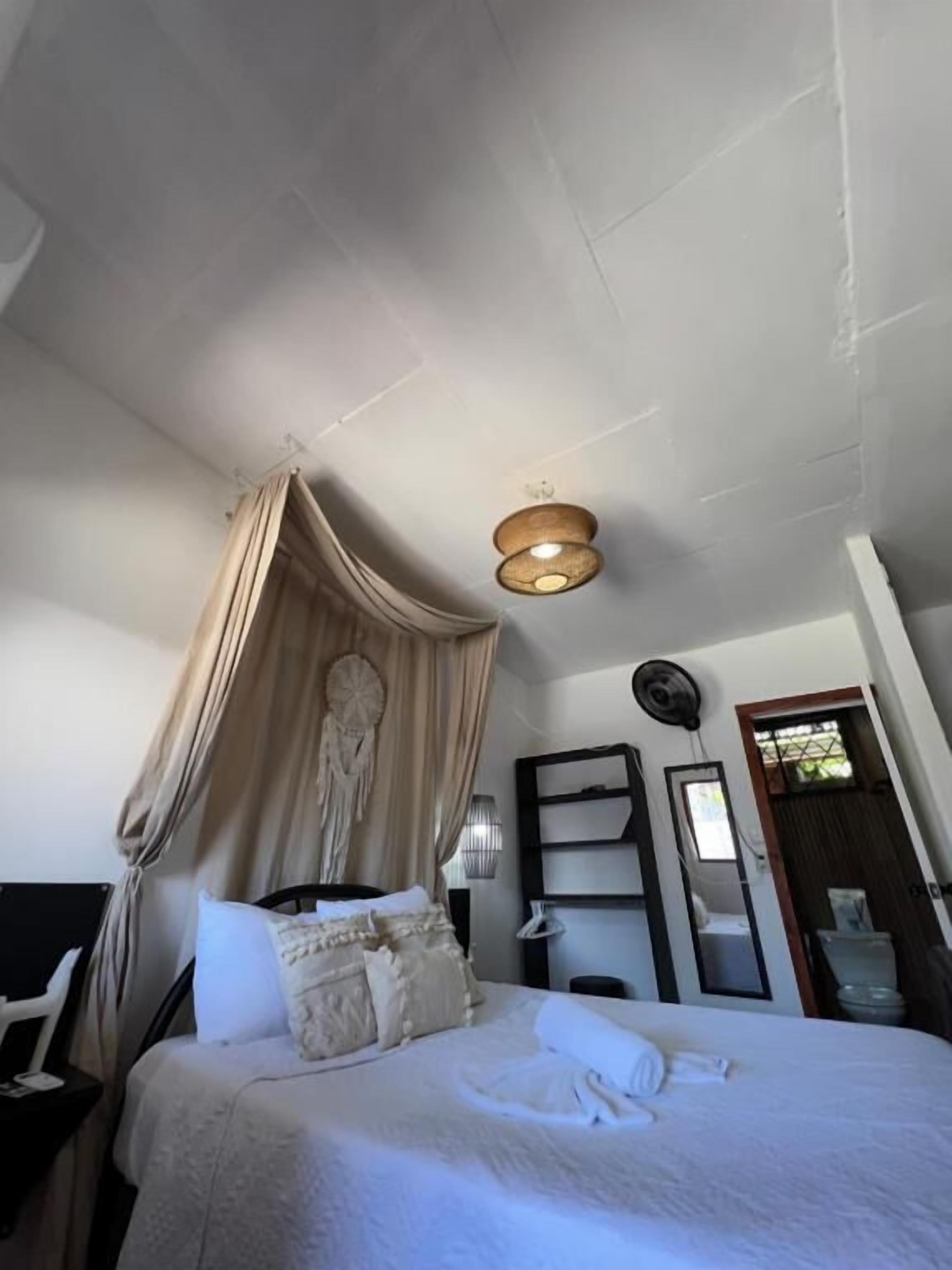 A bedroom with a canopy bed, a bedside table, a wall-mounted fan, and a mirror.