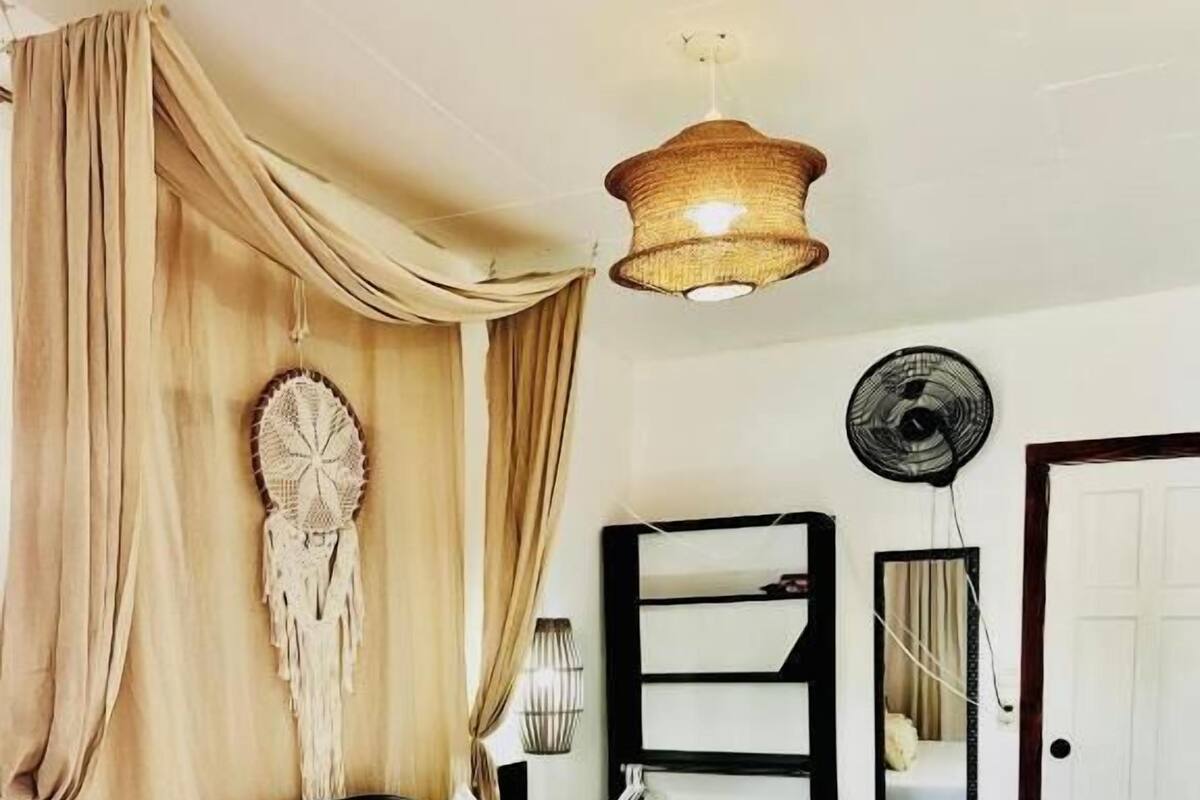 Un dormitorio con una cama, un atrapasueños colgante, un ventilador y un espejo en la pared.